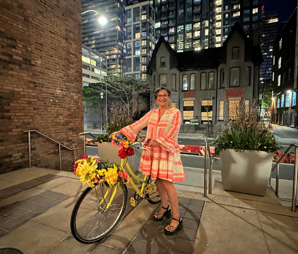 Ali wearing a bright dress posing with her bike at night.